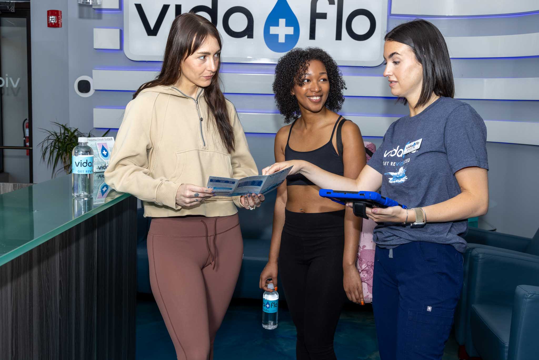 Two patients learning about vitamin boosters for IV hydration from a Vida-Flo Registered Nurse.